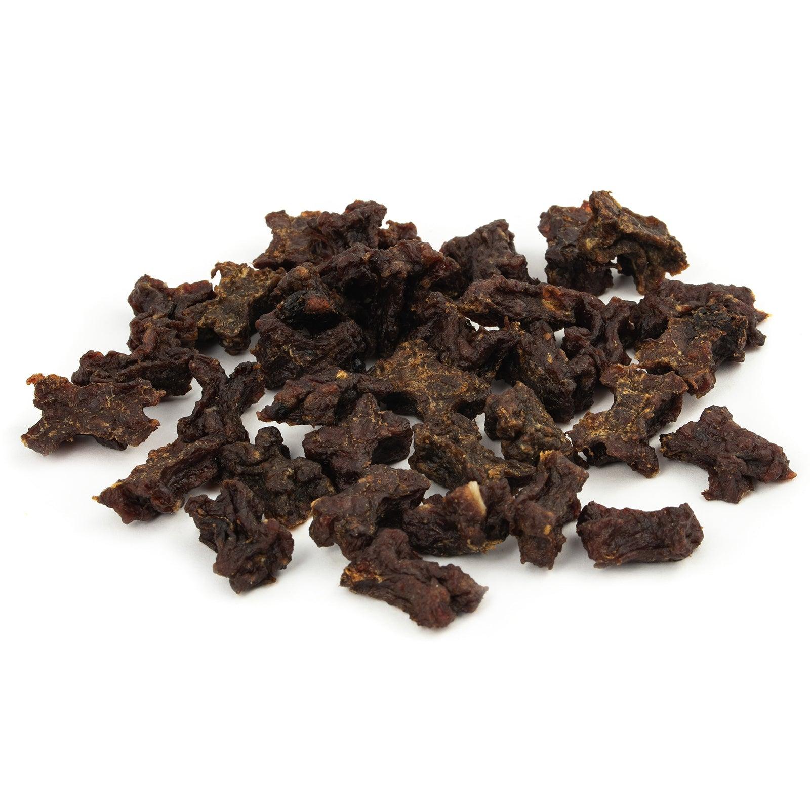 Pile of dark brown beef jerky pieces scattered on a white background, showing irregularly shaped dried meat chunks.